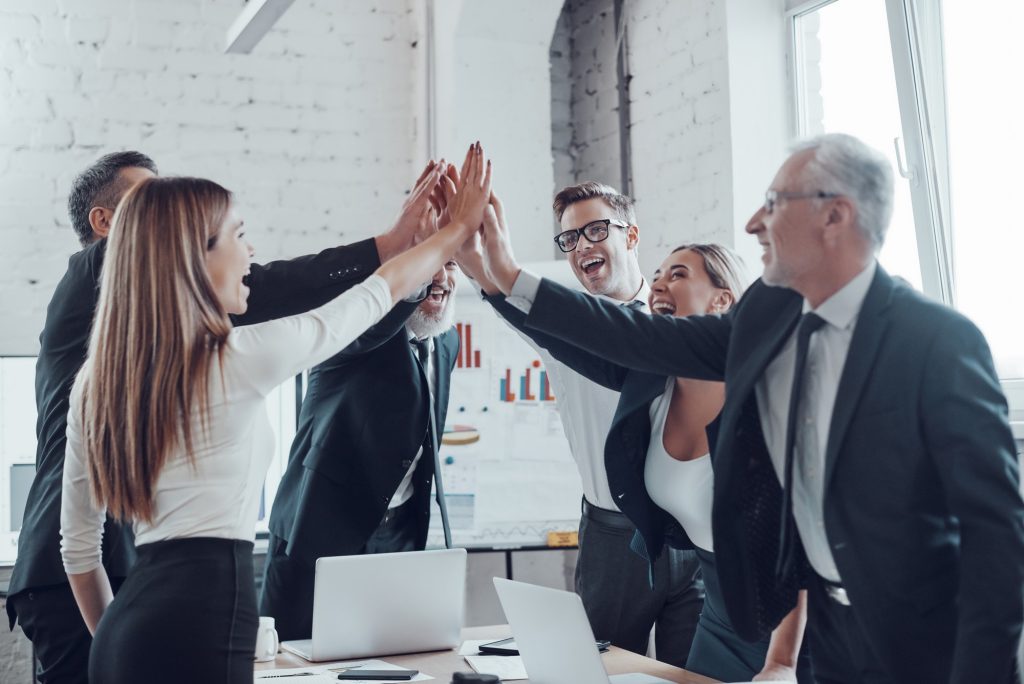 CG Panel et son équipe d'affaires joyeuse se tapant mutuellement les mains pour fêter la réussite dans un bureau moderne