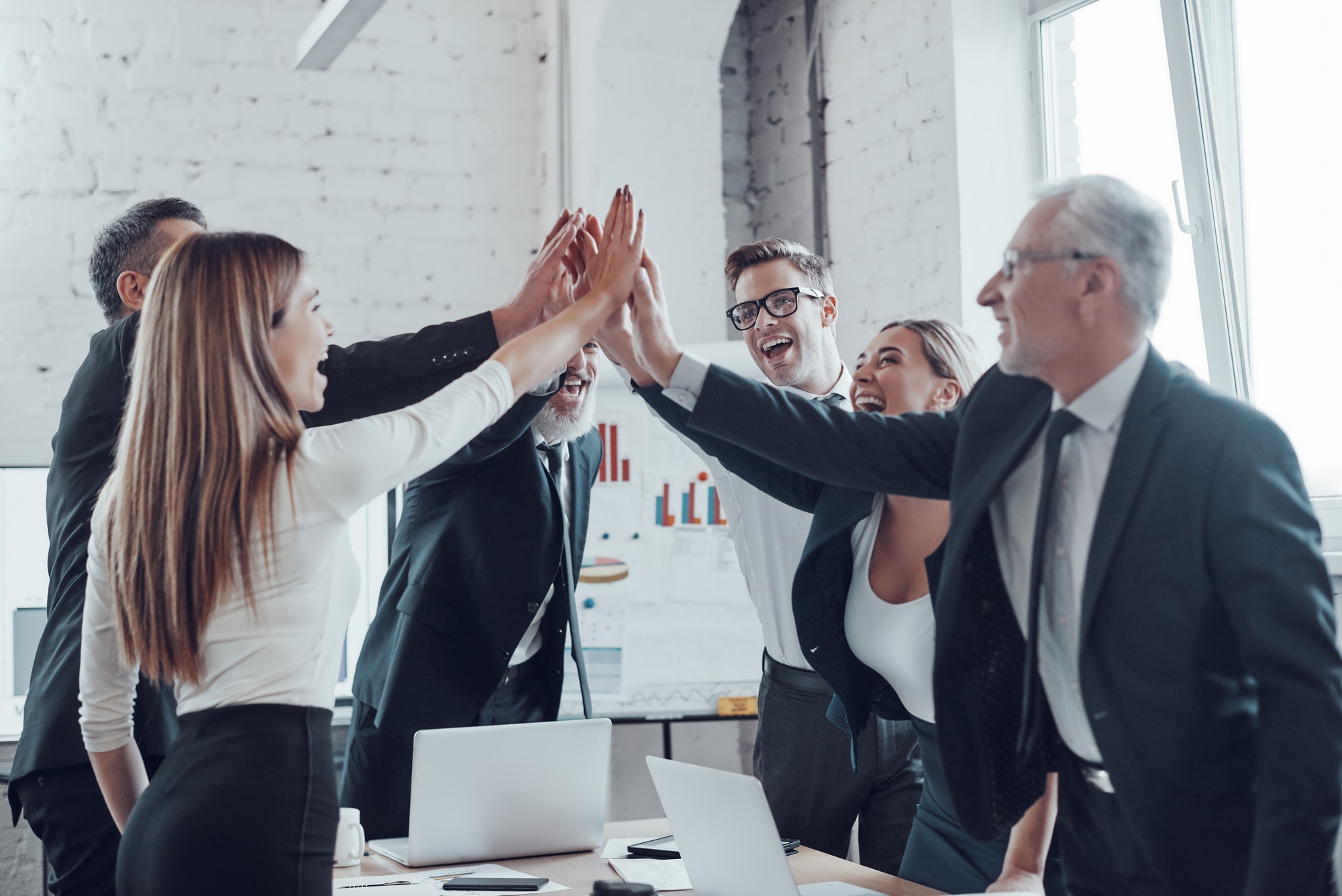 CG Panel et son équipe d'affaires joyeuse se tapant mutuellement les mains pour fêter la réussite dans un bureau moderne